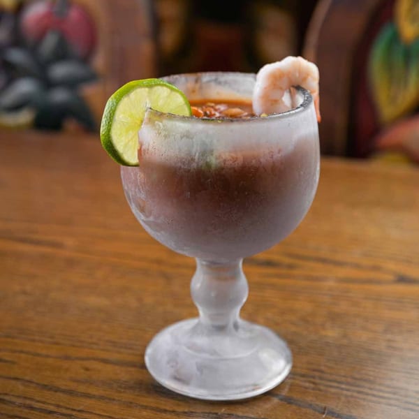 A frosty glass of Pecina's Mexican Cafe's Michelada, garnished with a lime wedge and a shrimp.