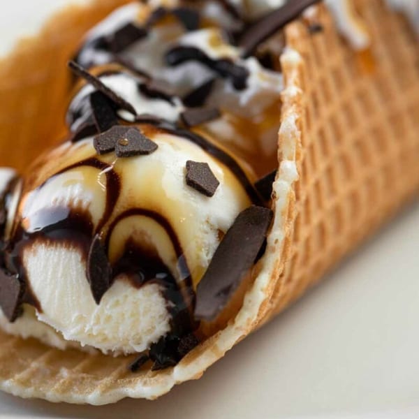 Vanilla ice cream in a waffle cone, drizzled with chocolate and caramel, topped with whipped cream.