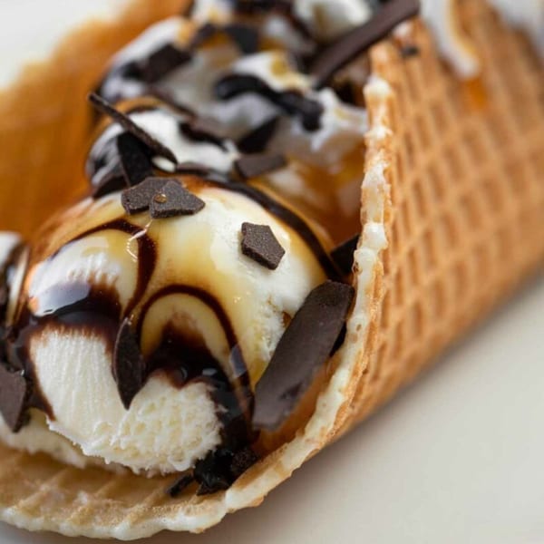 Waffle cone filled with vanilla ice cream, chocolate syrup, and chocolate shavings.