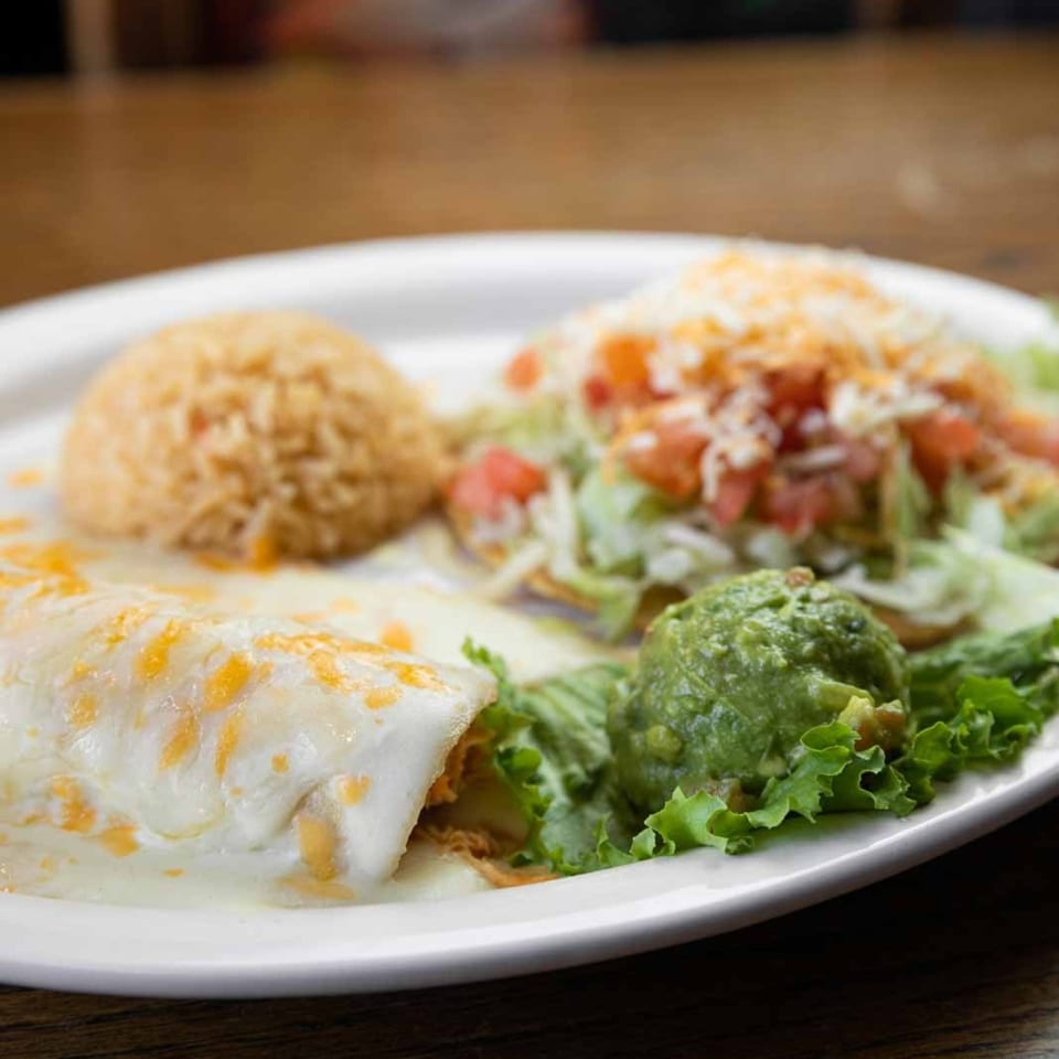 A Pecina's Mexican Cafe combo plate with a cheesy burrito, rice, tostada, and guacamole.