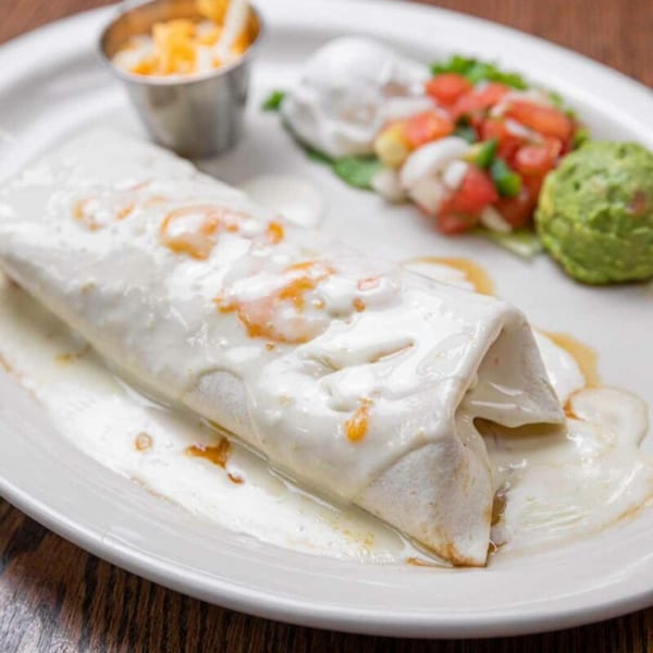 A Pecina's Mexican Cafe burrito covered in white sauce, with guacamole, pico de gallo, and cheese.