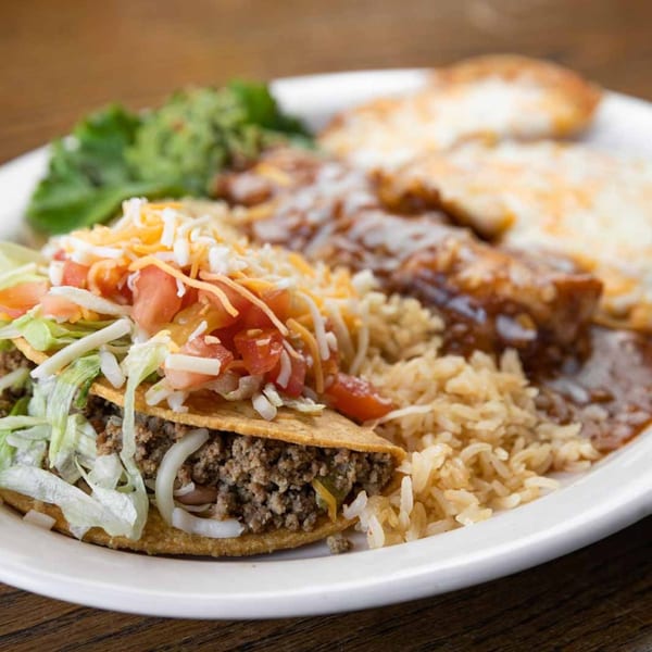 A Pecina's Mexican Cafe plate with a crispy taco, rice, enchiladas, and guacamole.