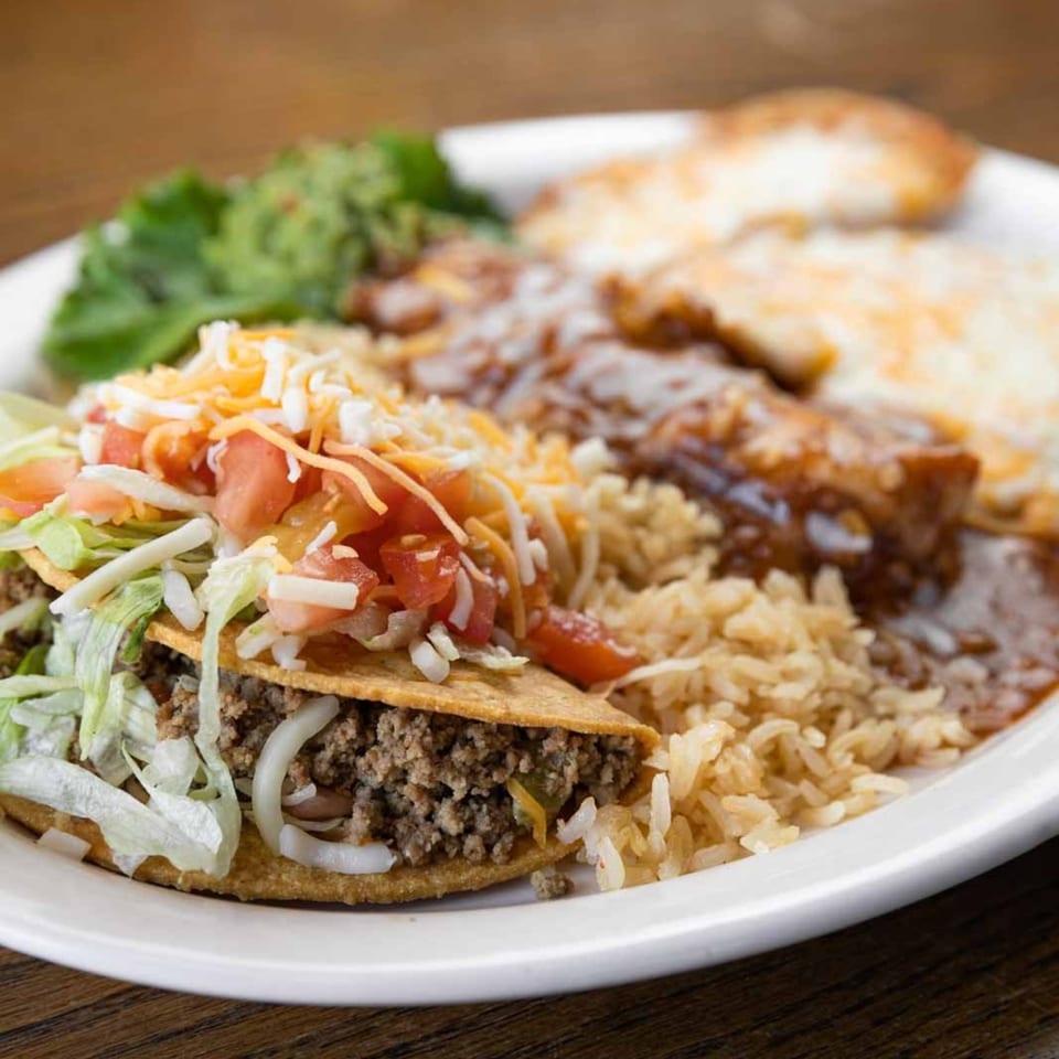 A Pecina's Mexican Cafe plate with a crispy taco, rice, enchiladas, and guacamole.