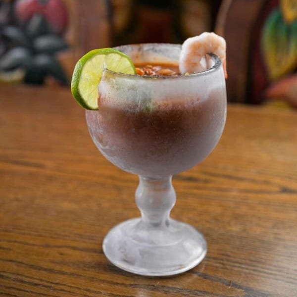 A frosty glass of Pecina's Mexican Cafe's shrimp cocktail, garnished with a lime and shrimp.