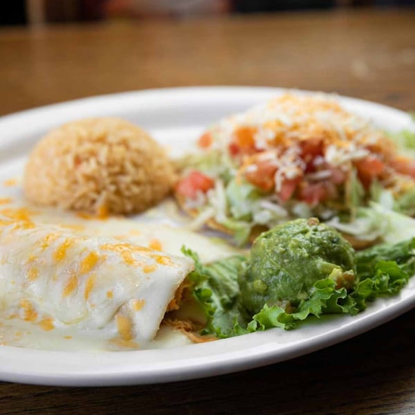 A Pecina's Mexican Cafe plate with a cheesy burrito, rice, guacamole, and a taco.