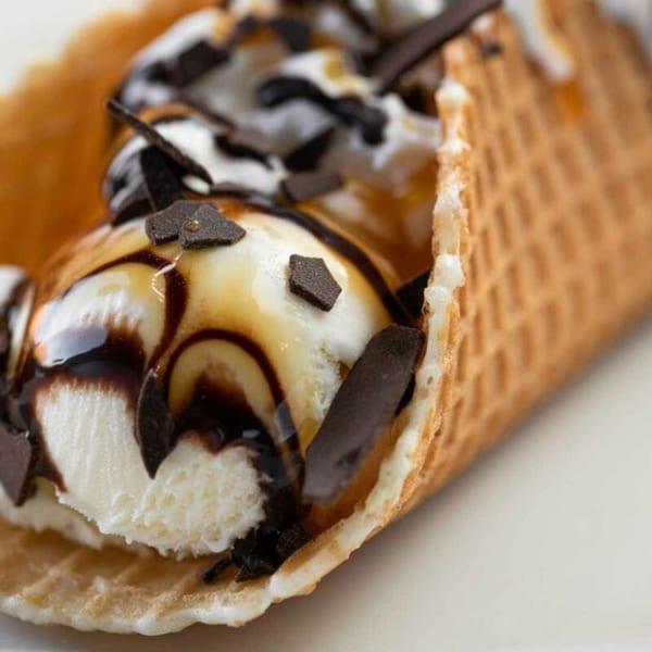 Waffle taco dessert with vanilla ice cream, chocolate syrup, and chocolate shavings.